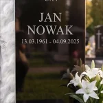 grawerowany napis na czarnym granicie nagrobka obok szklanego panelu z Jezusem