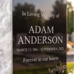 engraved headstone inscription in black granite next to glass memorial panel of Jesus