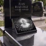 Placa conmemorativa de cristal con retrato y nombre y fechas sobre lápida de granito
