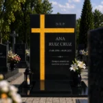 Cruz asimétrica de vidrio dorado pegada a una lápida de granito negro