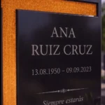 Cruz asimétrica de vidrio dorado pegada a una lápida de granito negro
