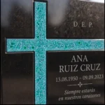 Cruz asimétrica de vidrio turquesa en una lápida de granito negro