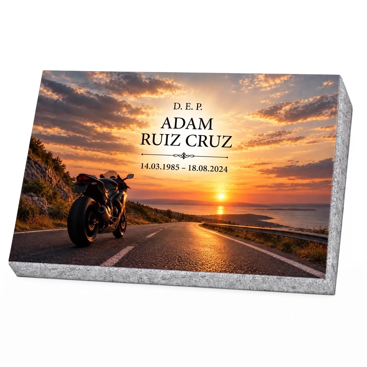 Placa conmemorativa de vidrio con una moto en una carretera junto al mar al atardecer, sobre base de granito